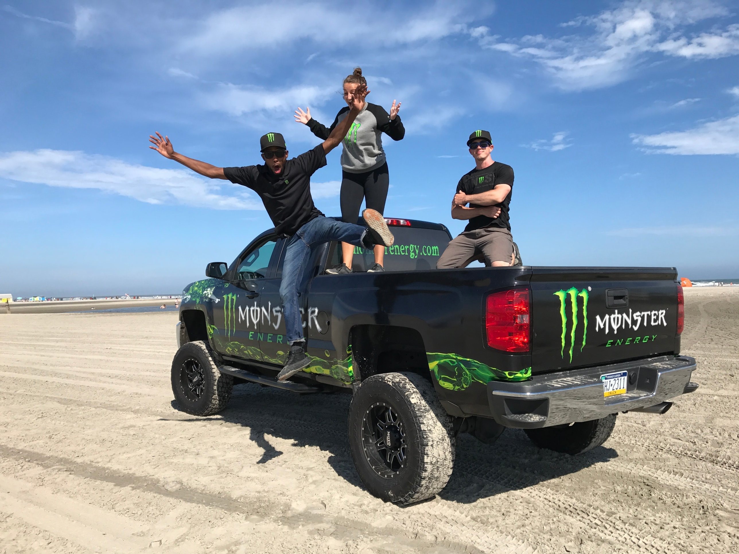 Davone leaping off a Monster Energy wrapped truck with the brand team on the beach